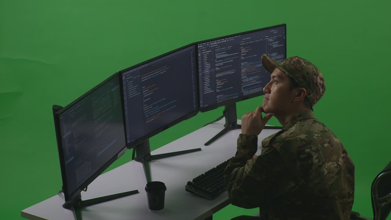 Side View Of Asian Man Soldier Developer Thinking About Something Then Raising His Index Finger While Write Code With Multiple Computer Screens In Green Screen Studio