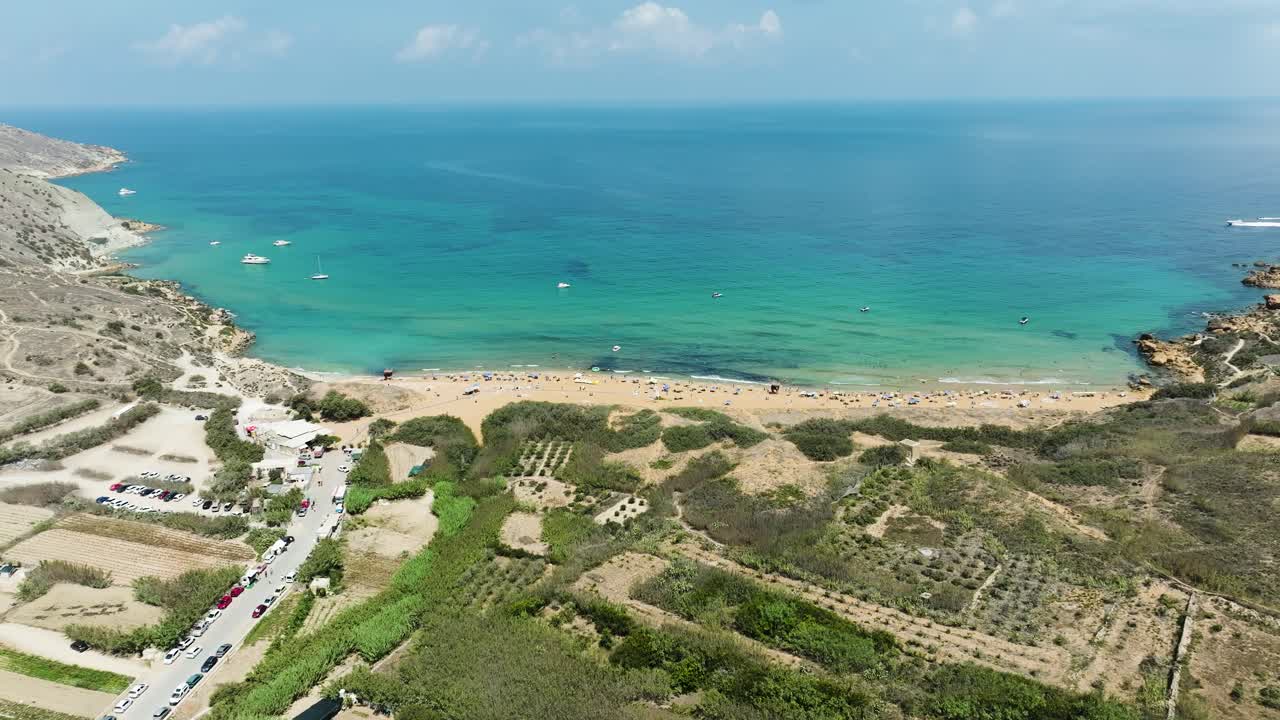 impresionantes imágenes aéreas de drones que muestran una playa de arena bordeada por aguas claras y tranquilas, con barcos y bañistas disfrutando de la soleada escena costera y el campo en el fondo