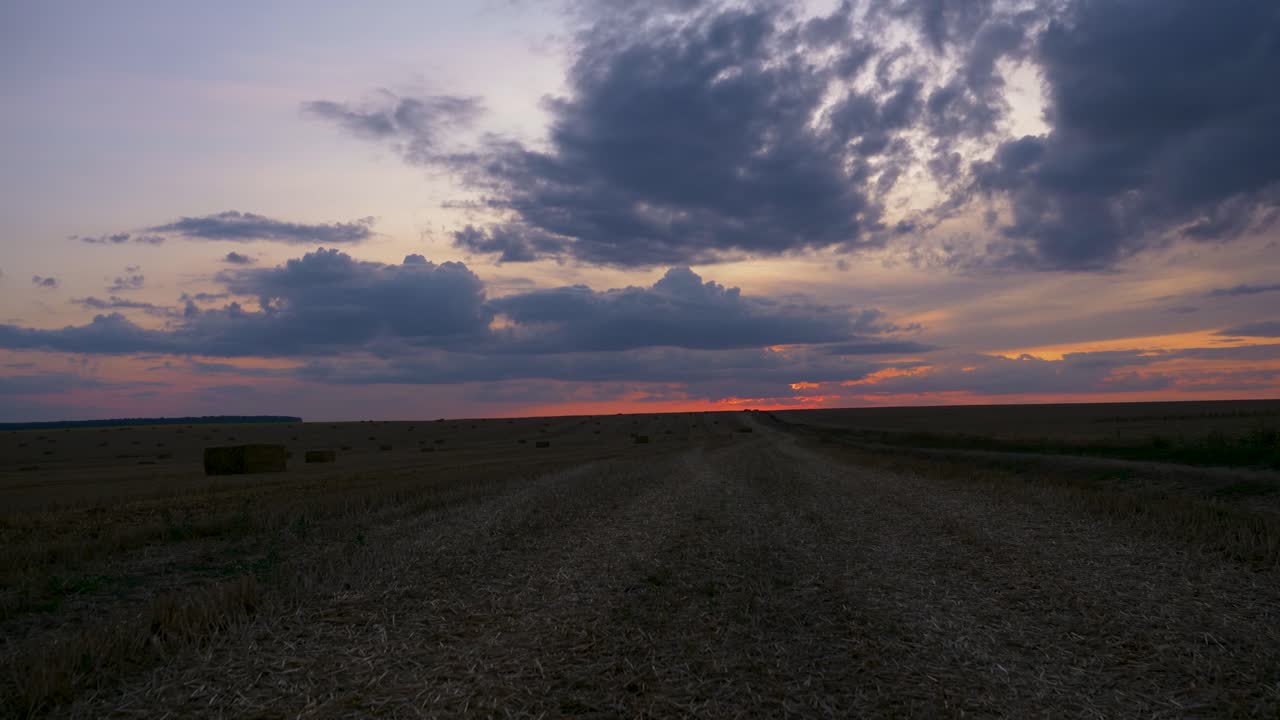 lapso de tiempo del cielo naranja nublado de la puesta de sol sobre el campo de cosecha con pajar