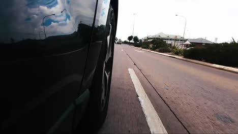 Car-POV-from-road-facing-front-right-wheel-driving-down-bitumen-road-down-a-hill-into-town