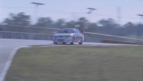 Un-Coche-De-Carreras-Corre-Alrededor-De-Una-Pista-Mientras-La-Gente-Mira