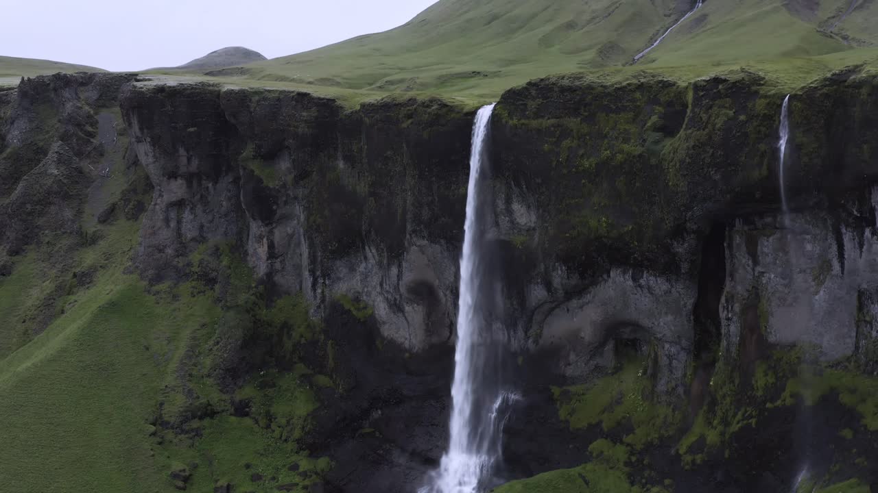 corriente de agua blanca fluye desde el borde de un acantilado escarpado en un paisaje verde