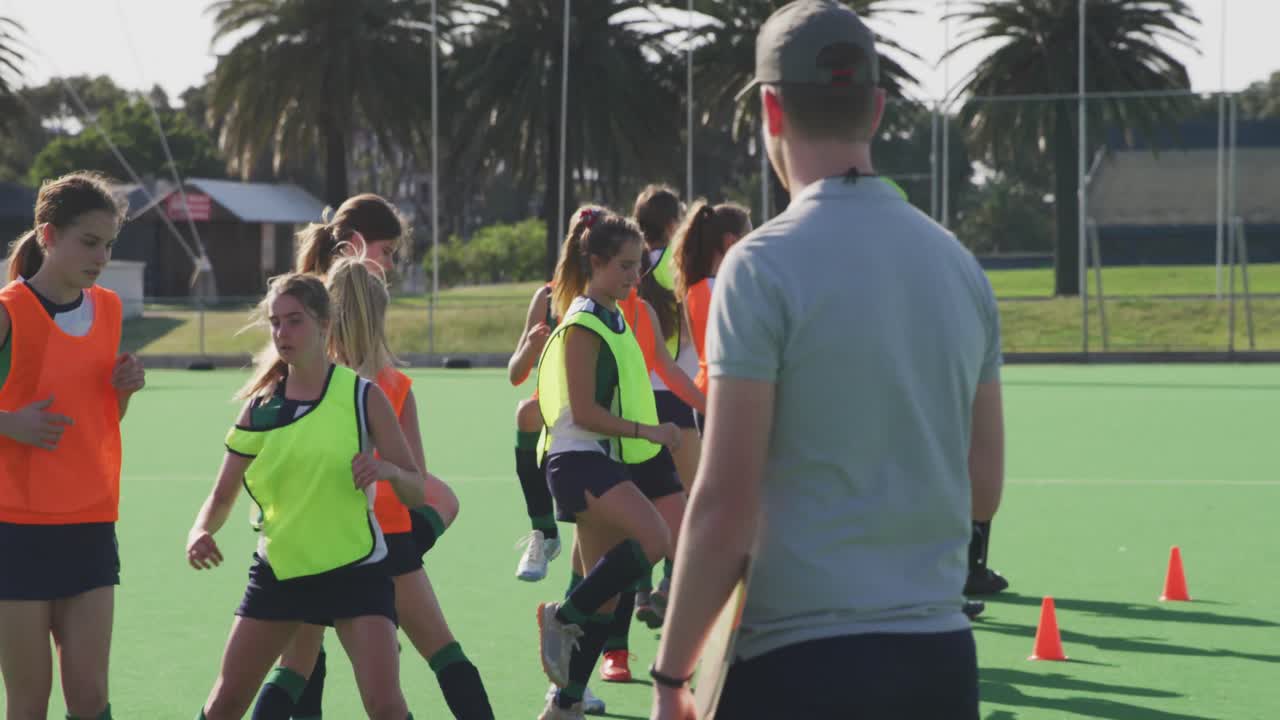 여자 하키 선수 들 이 경기장 에서 운동 을 하는 것 을 지켜보는 코치