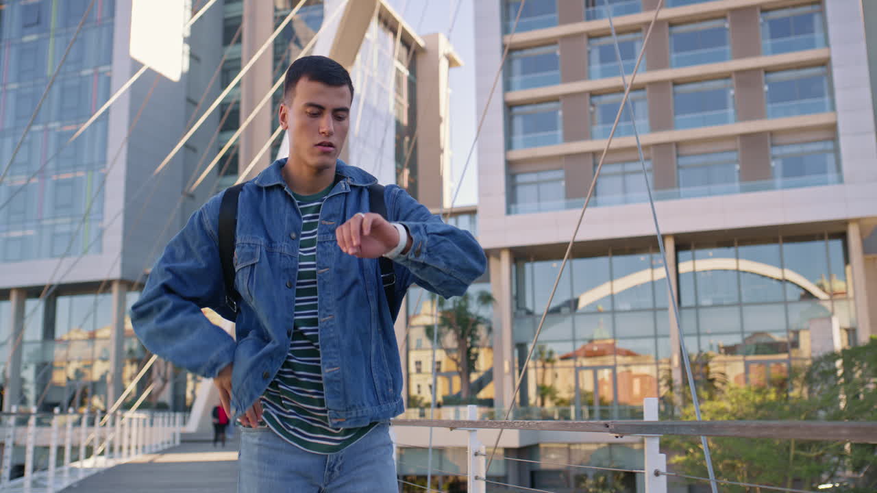 Man in denim jacket checking the time on a city bridge