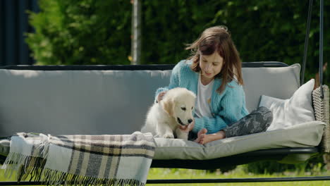 a child plays with a cute golden retriever puppy. sitting on a garden swing in the backyard of a house