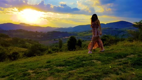 Sonnenuntergang-über-Den-Bergen-Mit-Einem-Mädchen,-Das-Vor-Freude-Auf-Einem-Grasbewachsenen-Hügel-Tanzt-Und-Sich-Dreht