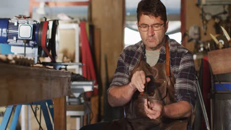 Caucasian-male-knife-maker-sitting-in-workshop,-holding-and-checking-knife