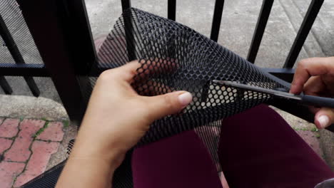 hands of a person cutting a mesh plastic net with scissors