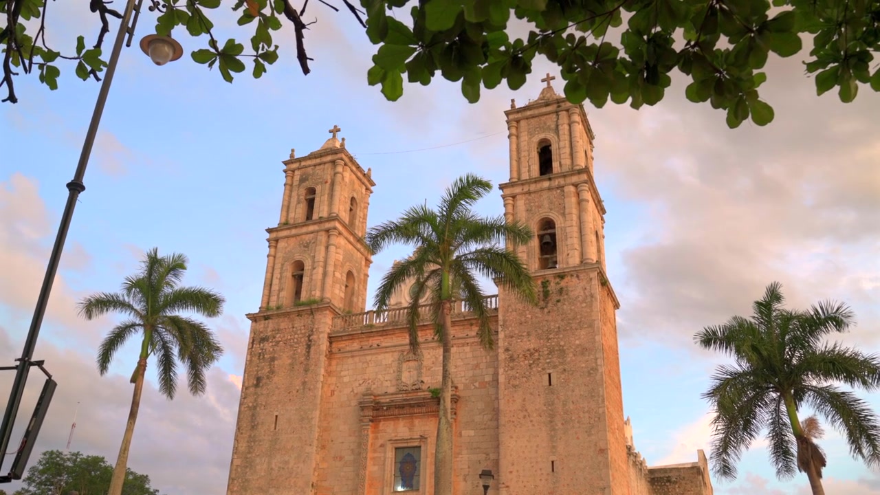 Meksika'nın Yucatan eyaletindeki Valladolid şehrinde, gün batımında palmiye ağaçlarıyla çevrili tarihi San Servacio Kilisesi cephesinin alçak açıdan görünümü.