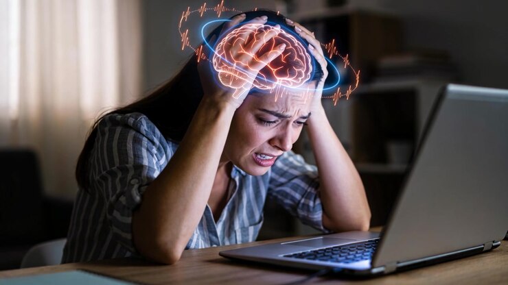 Gripping temples, woman in striped shirt reacting to laptop work at desk, glowing brain overlay