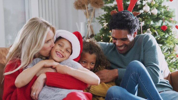 Parents Tickling Children As Family Sit On Sofa Celebrating Christmas Together