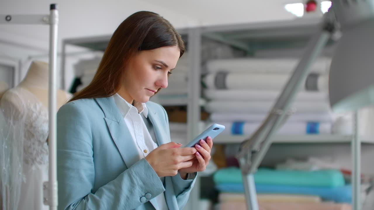 una joven diseñadora con un teléfono móvil en un taller de costura escribe mensajes a los clientes. comunicación con clientes de pequeñas empresas.