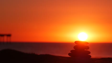 stack of pebble stones, sandy ocean beach, sunset sky. rock balancing by water.