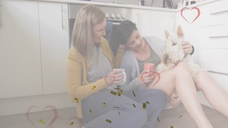 Animation-of-hearts-and-confetti-over-caucasian-female-couple-sitting-on-floor-with-their-pet-dog