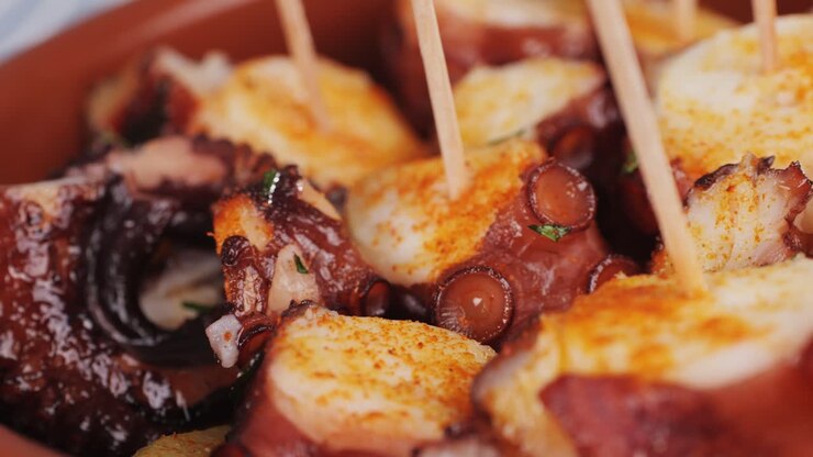 Cottura del polpo: chef griglia polpo fresco alla galiziana nella cucina di un ristorante. Cibo sano, specialità di mare in Spagna. Piatto tradizionale asiatico, giapponese, spagnolo e mediterraneo.
