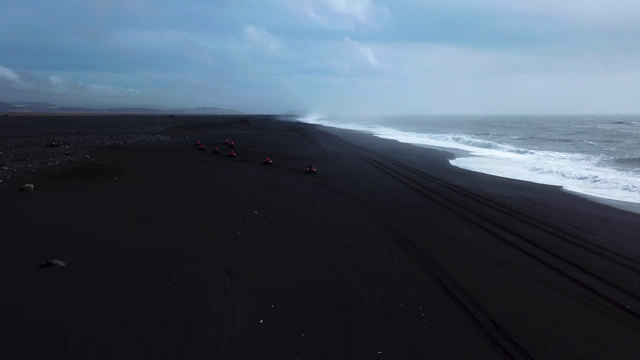 Aerial view of red quad bikes speeding off road on Iceland black sand beach, next to the ocean