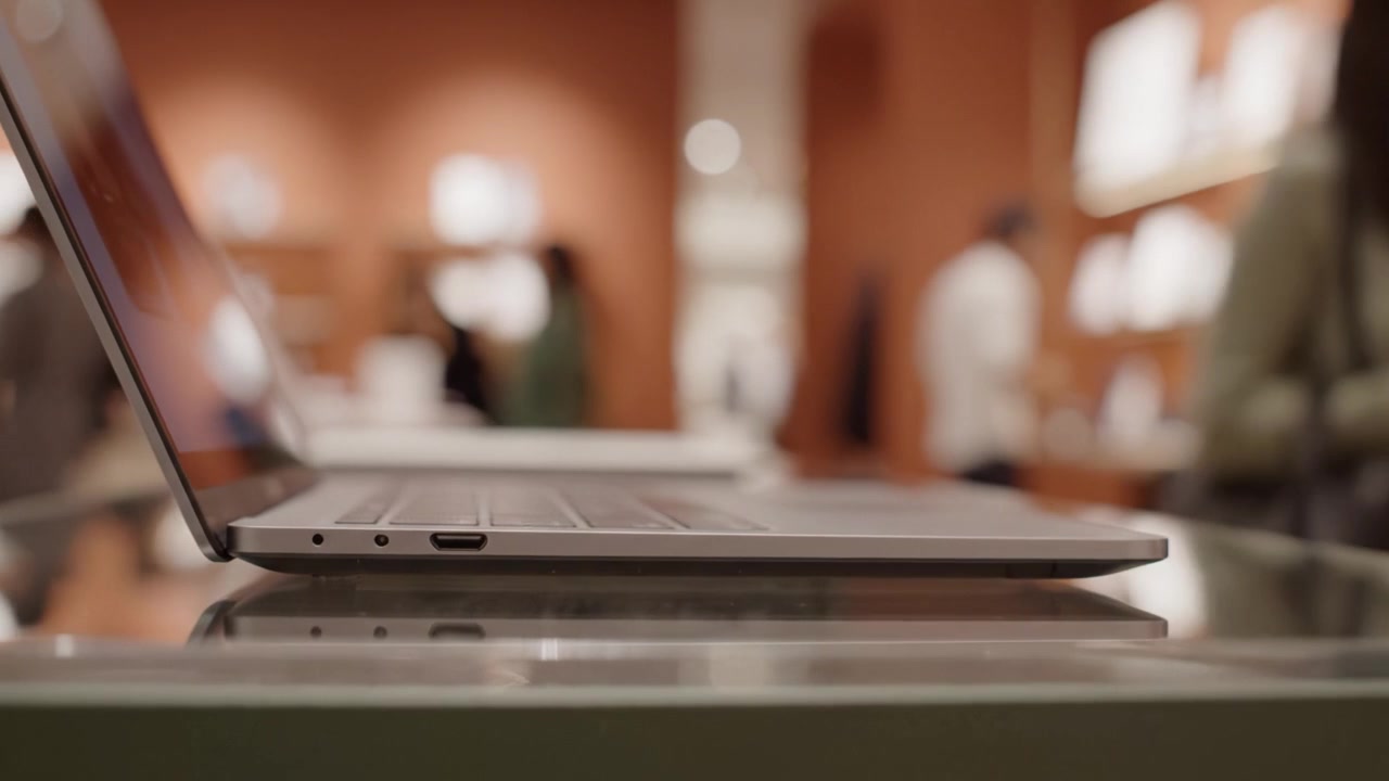 Laptop elegante esposto in un moderno ambiente di vendita al dettaglio con clienti sfocati sullo sfondo e un'elegante disposizione dei prodotti che migliora l'esperienza digitale