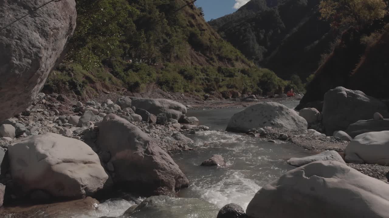 río rocoso que serpentea a través de las montañas en el valle del cañón agua que fluye acercándose a rocas grises árboles verdes cielo azul y nubes antena rápida avanzando proximidad