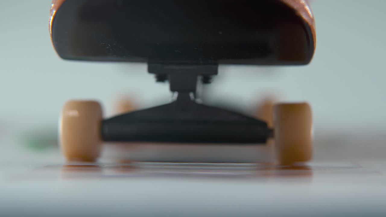 гипер крупный макро подробный снимок мини-скейтборда, крошечные белые колеса, езда на пальце, скольжение пальцев вперед и назад перед камерой, профессиональное освещение, статическое кинематографическое 4k видео