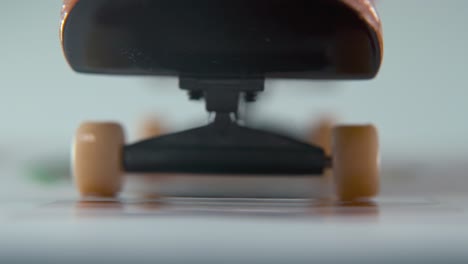 un macro de primer plano detallado de un mini skateboard, pequeñas ruedas blancas, montar en tablero de dedos, deslizar el dedo hacia atrás y hacia adelante frente a la cámara, iluminación profesional, vídeo estático cinematográfico 4k