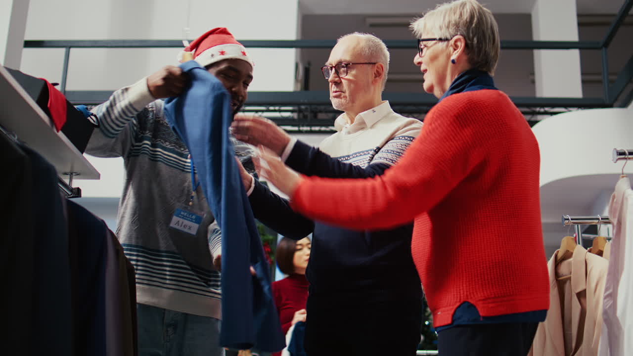 Elderly couple in festive adorn shopping mall fashion boutique, being helped by friendly retail assistant with finding ideal outfit during Chrismas holiday season promotional sales