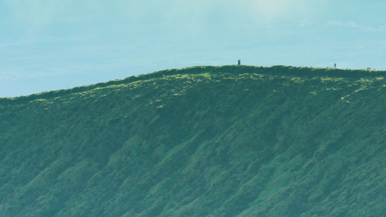 아조레스(azores) 칼데이라 화산 가장자리를 따라 걷는 두 명의 조깅하는 사람의 극적인 긴 렌즈 샷
