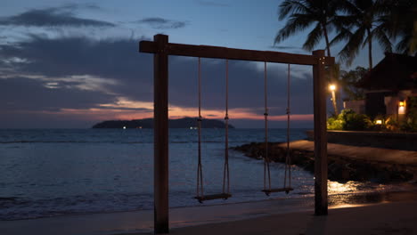 Columpio-De-Cuerda-De-Playa-De-Pareja-Vacía-Al-Atardecer-Frente-Al-Mar-Cerca-De-Bungalow-Exótico-Con-Palmeras-Altas