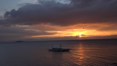 puesta de sol sobre el océano en filipinas con una pequeña isla al fondo y un barco tradicional filipino en primer plano