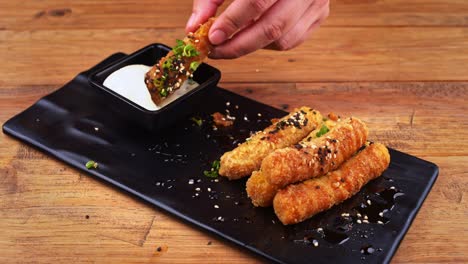 close up of a plate of breaded cheese fingers with sesame seeds, habanero peppers, ranch dressing and worcestershire sauce, cheese finger being dipped in ranch dressing