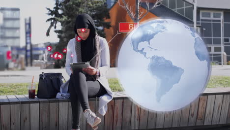 globo y múltiples iconos digitales flotando sobre una mujer en hijab usando una tableta digital en la calle