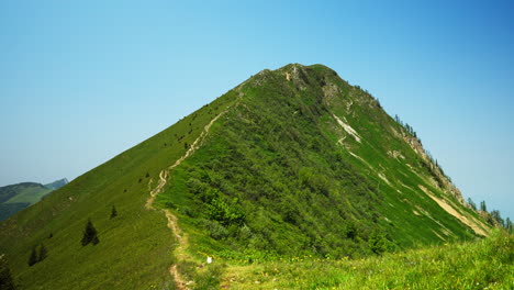 a stunning ridgeline trail near golica, slovenia, with steep grassy slopes on both sides. the narrow mountain path across a green crest with forested hills and peaks stretching far into the horizon.