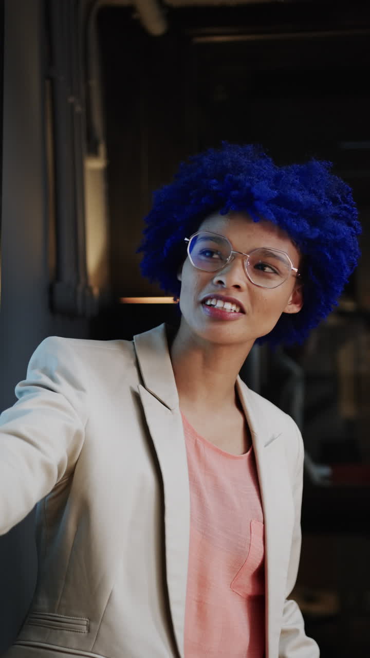 Vertical video of biracial businesswoman with blue afro having presentation in office, slow motion