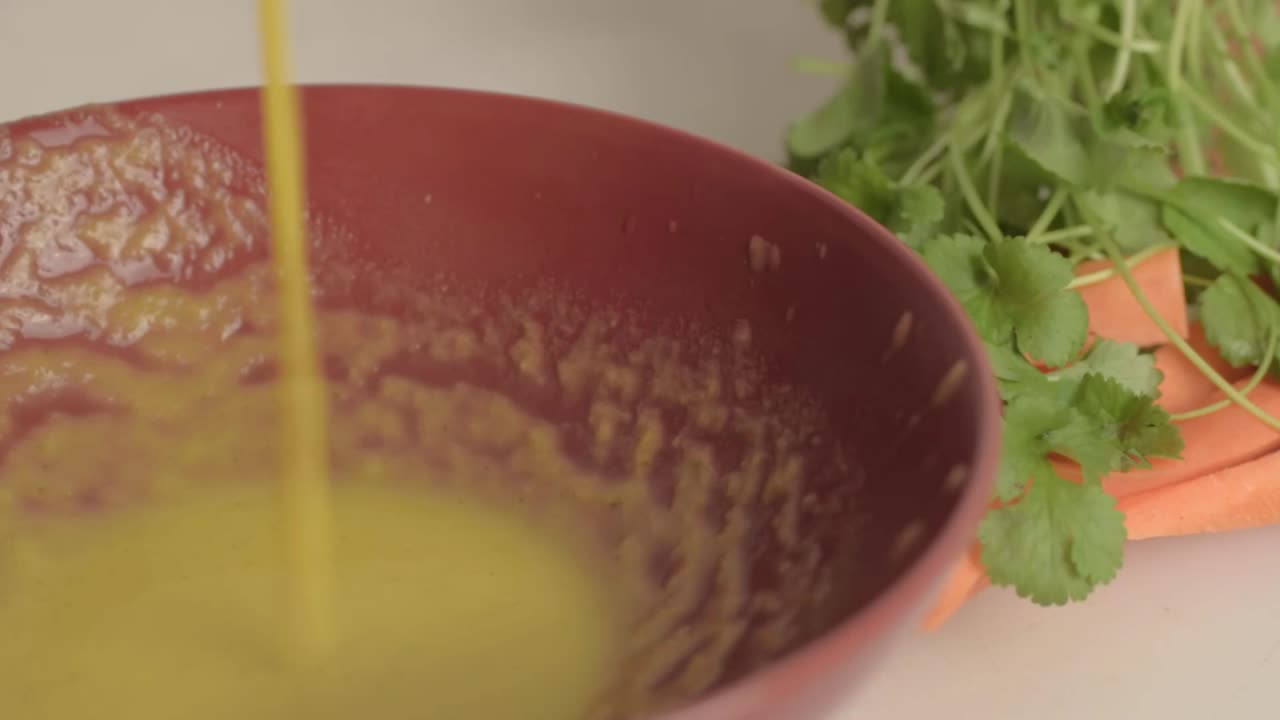 Pouring fresh carrot and coriander soup into a bowl close up
