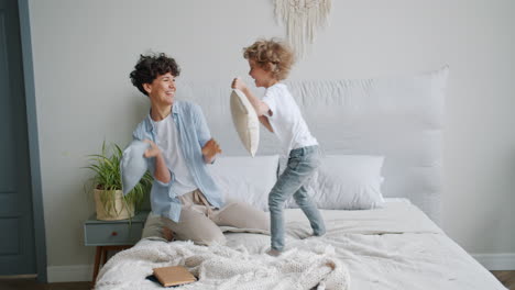 mother and son having fun pillow fight on bed