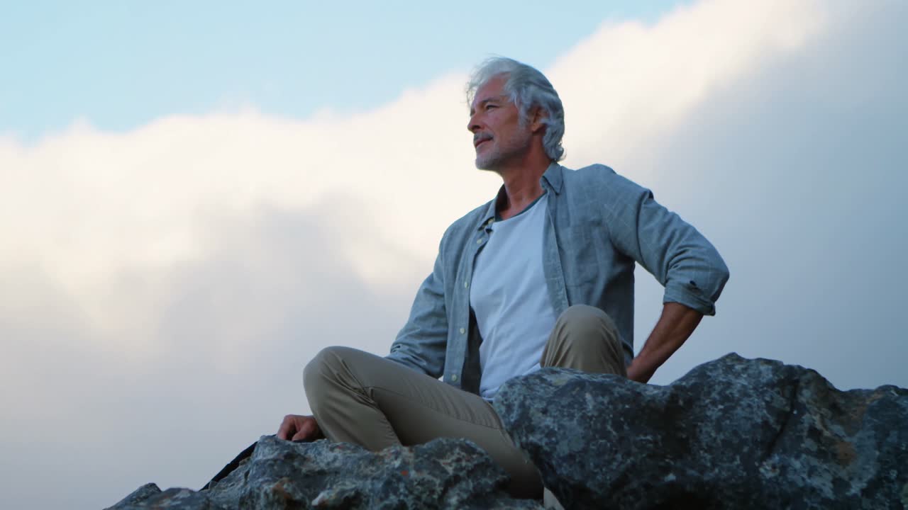 Senior man relaxing on a rock at countryside 4k