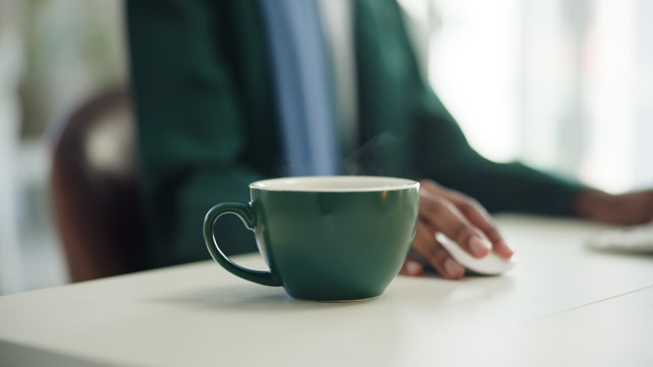 仕事中の人がいるオフィスデスクの上の湯気の立つコーヒーカップ