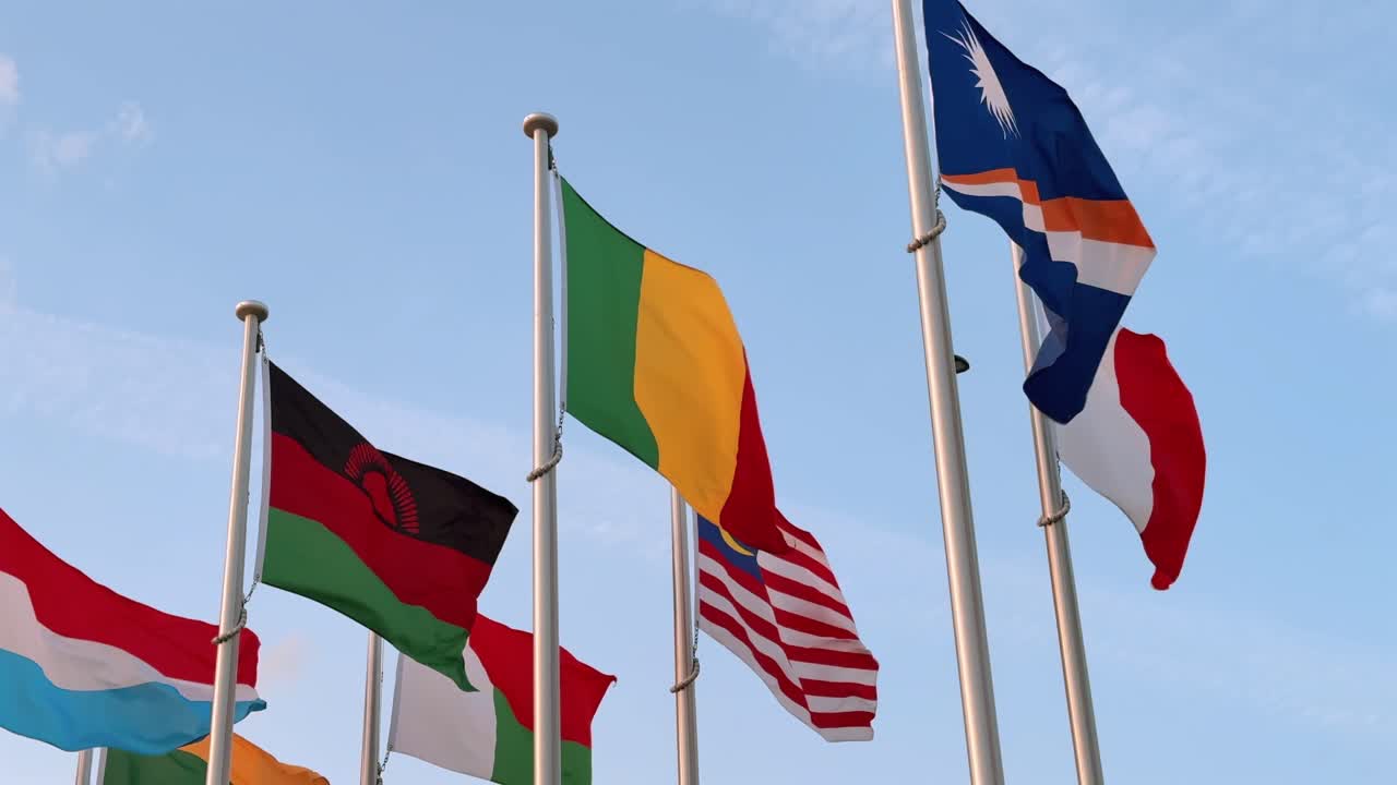 Seven national flags wave gracefully together in the breeze, symbolizing global unity, diversity, and shared presence on the world stage under a bright sky