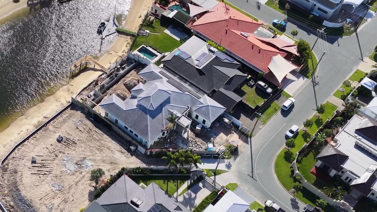 High-angle drone shot reveals upscale canal homes and active construction in a coastal neighborhood.