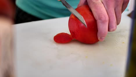 cutting a red tomato on cutting board with a dull knife