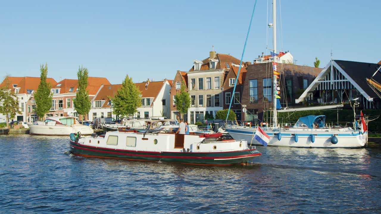 Sailboat passes raised canal bridge and historic Dutch buildings in Haarlem, Netherlands, on sunny day