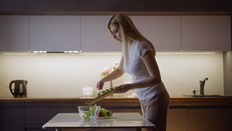 lady pours cut cucumbers into glass bowl at table in kitchen