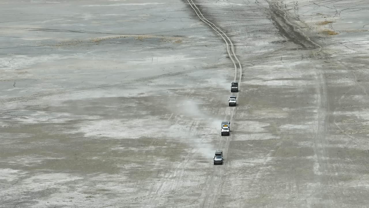 Aerial: Off-road expedition vehicles kick up dust on flat, arid plains