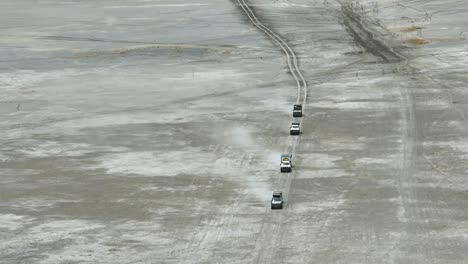 aerial: off-road expedition vehicles kick up dust on flat, arid plains