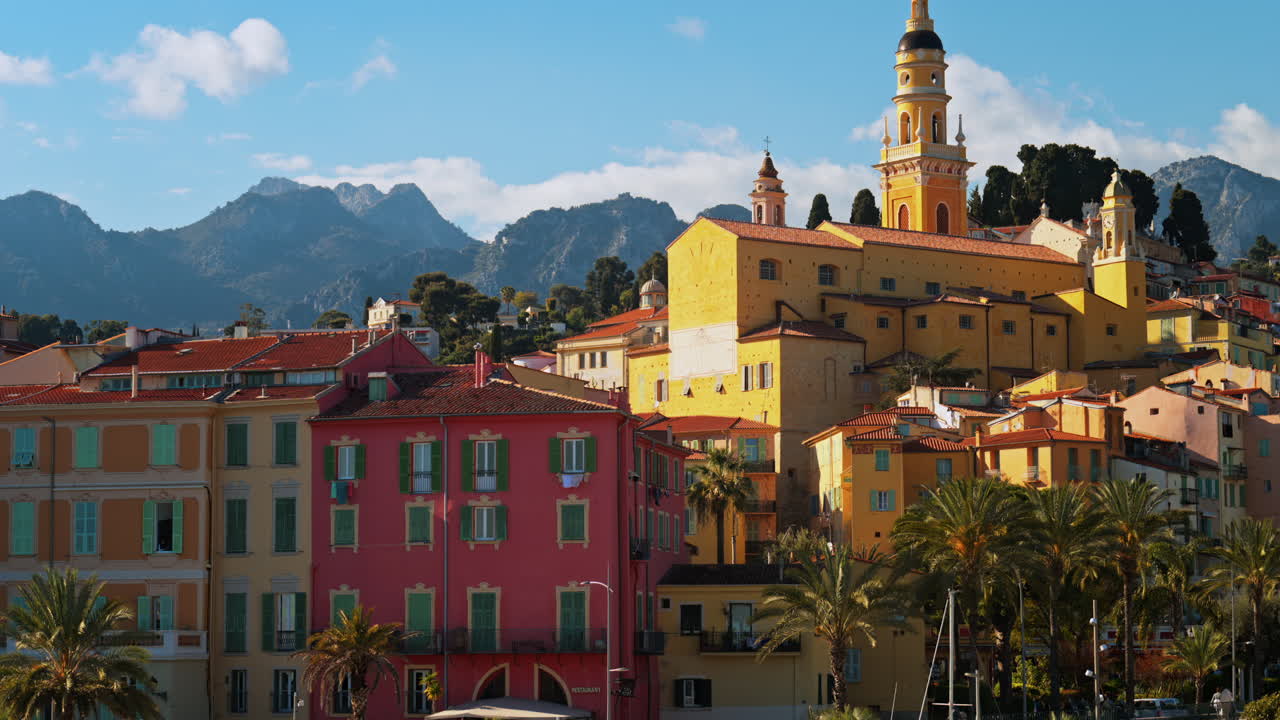 Distant view of the St Michel Basilica surrounded by colourful buildings and palm trees, Menton, France