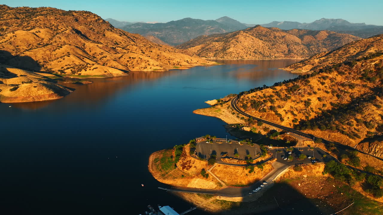Amazing sunlit scenery of the lake surrounded by sloping rolled mountains. Drone approaching the parking lot and observation deck on the rock.