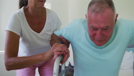 caucasian senior woman helping her husband walk using walking frame at home