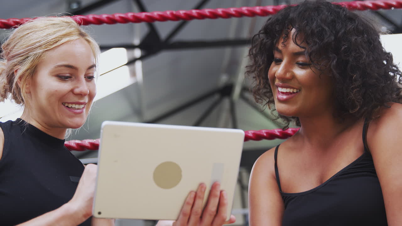 Female Personal Trainer With Female Boxer In Gym Checking Performance Using Digital Tablet