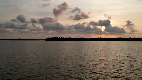 Bella-Toma-Aérea-De-Un-Lago-Vembanadu-Remanso,-Puesta-De-Sol,-Cocoteros,-Transporte-De-Agua,-Nubes,-Líneas-De-Agua,-Crepúsculo