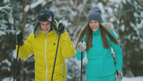 hombre sonriente con una chaqueta de invierno esquiando en el bosque a cámara lenta con su amada esposa. estilo de vida saludable. pareja joven