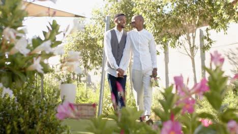 Glückliches-Afroamerikanisches-Schwules-Männliches-Paar,-Das-Hände-Und-Blumen-Bei-Der-Hochzeit-Hält,-Zeitlupe